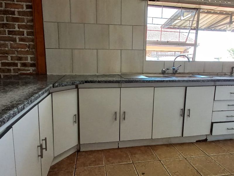 A functional kitchen featuring granite-look countertops, double stainless steel sink, white cabinetry, and a rustic exposed brick wall, ready for modern updates.