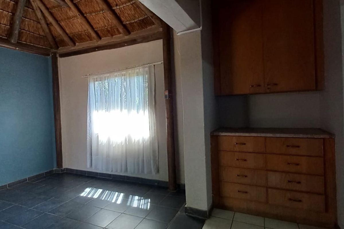 An empty living area featuring a traditional thatched roof with exposed timber beams, tiled flooring, and built-in wooden storage cabinetry.