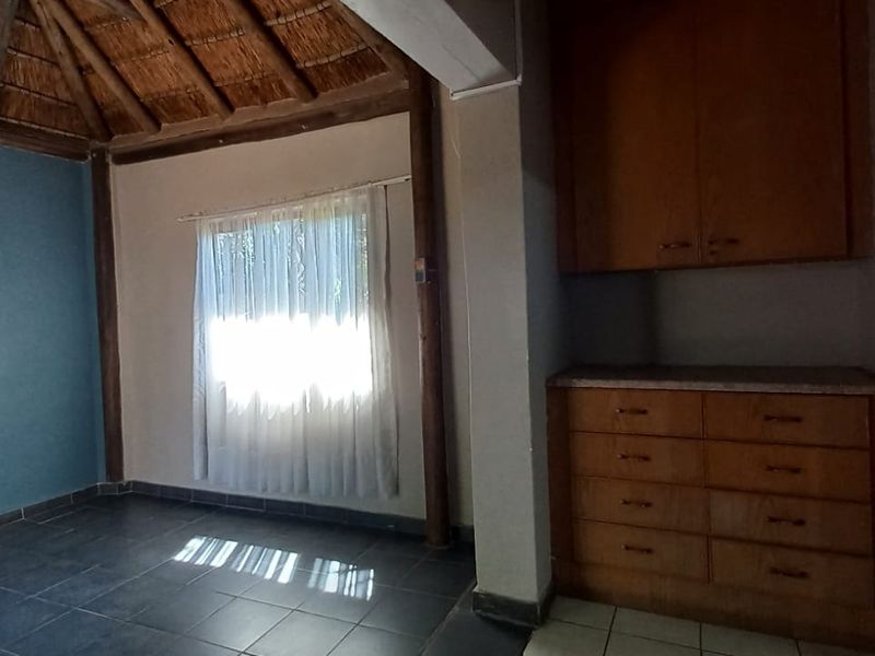 An empty living area featuring a traditional thatched roof with exposed timber beams, tiled flooring, and built-in wooden storage cabinetry.