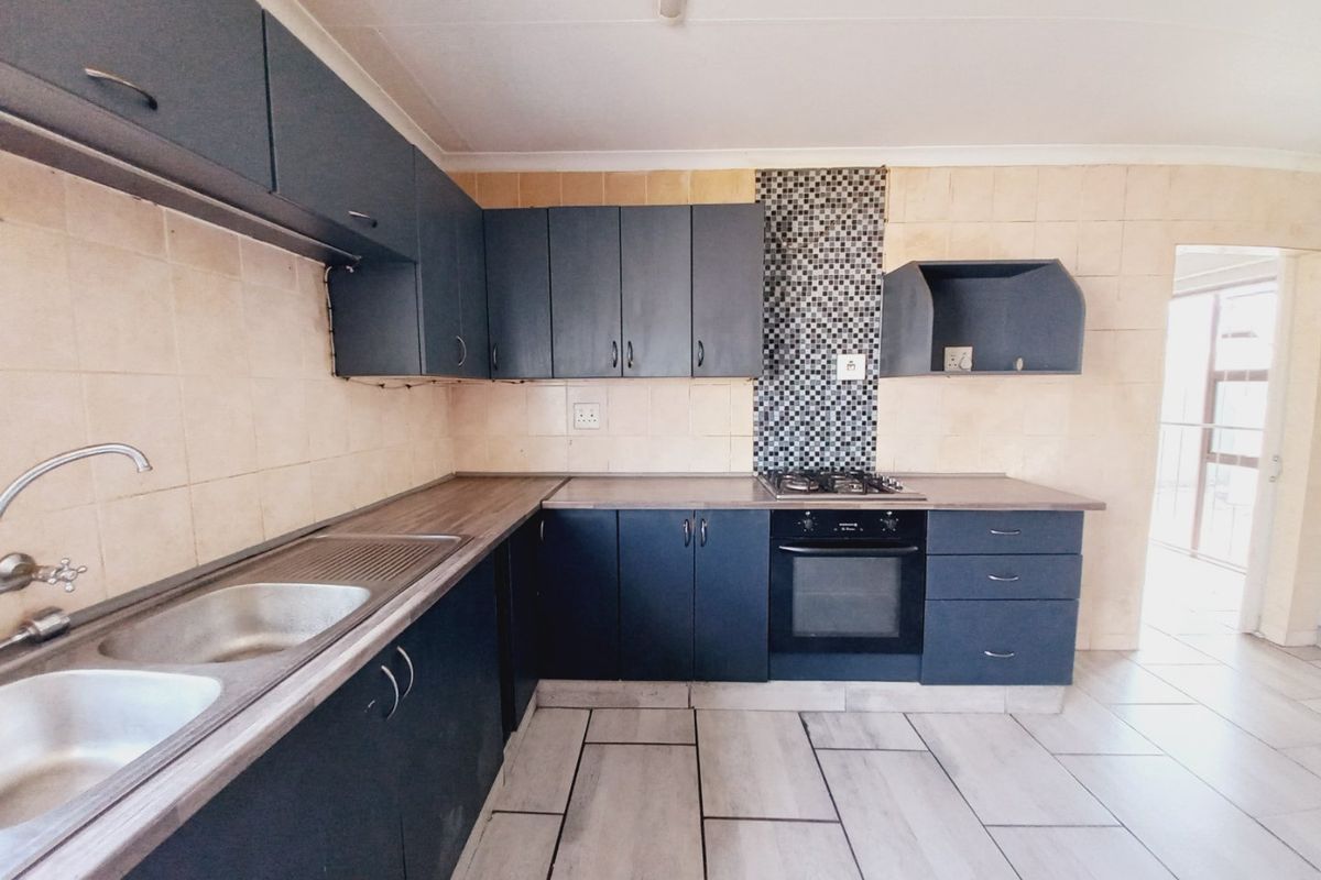 A functional kitchen featuring dark built-in cabinetry, laminate countertops, a gas hob, and a double bowl stainless steel sink with tiled splashbacks.
