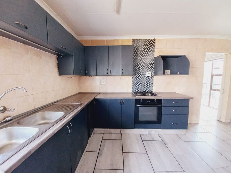 A functional kitchen featuring dark built-in cabinetry, laminate countertops, a gas hob, and a double bowl stainless steel sink with tiled splashbacks.