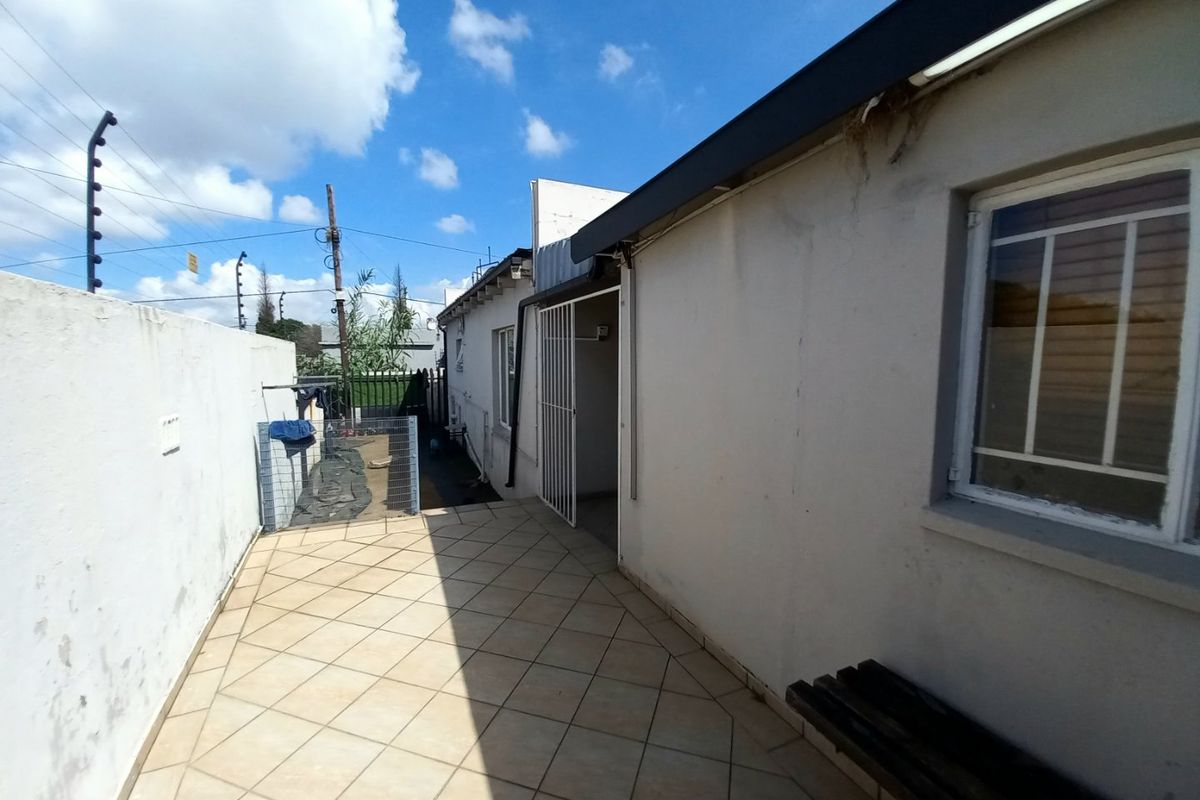 A paved rear patio area featuring a security gate, boundary wall with electric fencing, and exterior access to the apartment.