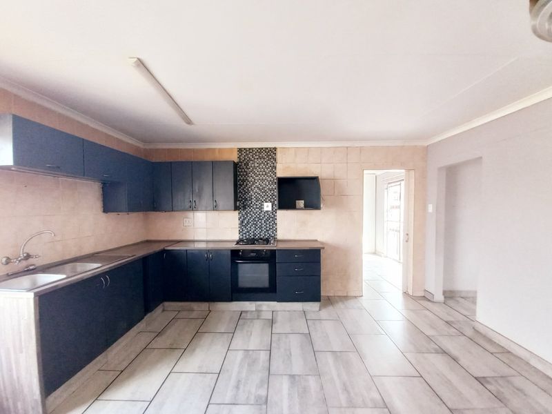 A functional kitchen featuring dark built-in cabinetry, a gas hob, built-in oven, and neutral ceramic floor tiles in an open-plan layout.