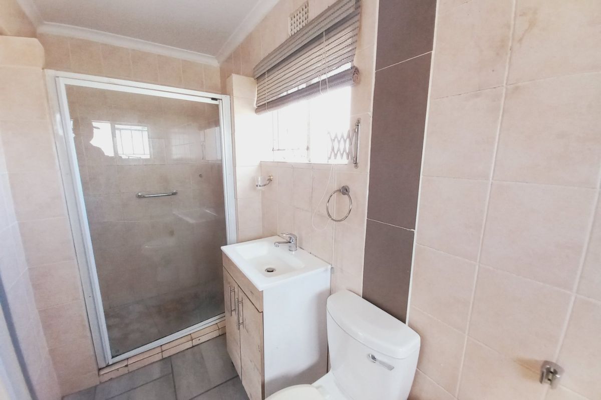 A functional bathroom featuring a shower enclosure, vanity cabinet with basin, and toilet, finished with neutral wall and floor tiling.