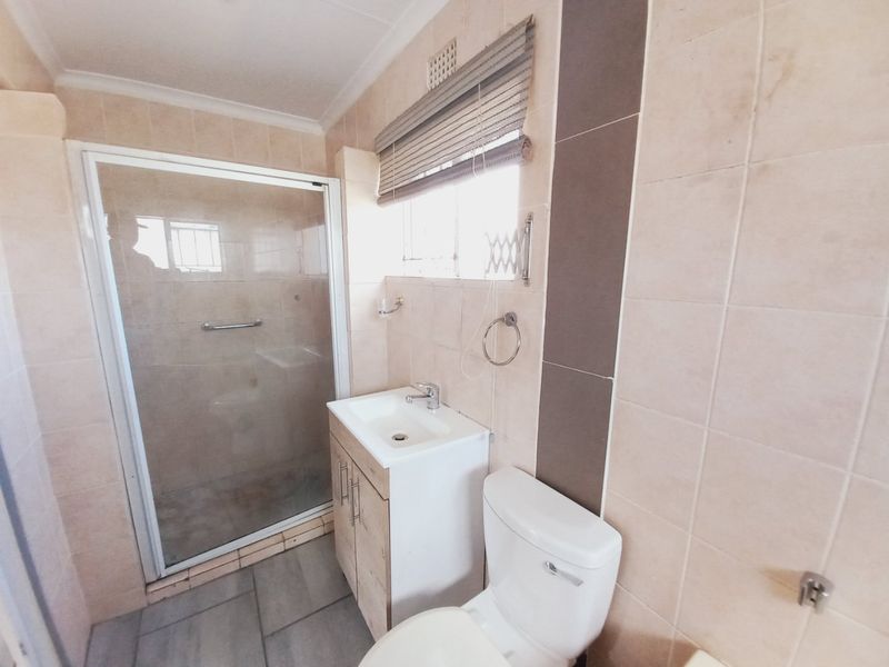 A functional bathroom featuring a shower enclosure, vanity cabinet with basin, and toilet, finished with neutral wall and floor tiling.