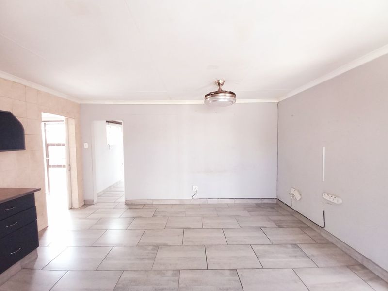 An empty open-plan living area featuring tiled flooring, a ceiling fan, and partial kitchen cabinetry, offering a blank canvas for interior design.