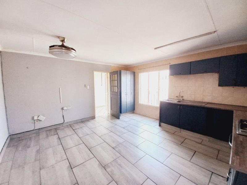 Open-plan living and kitchen area featuring tiled flooring, dark cabinetry, and a ceiling fan, offering a blank canvas for renovation.