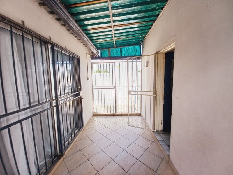 A covered outdoor patio area featuring tiled flooring, security gates, and protective window bars, providing a secure transition space.