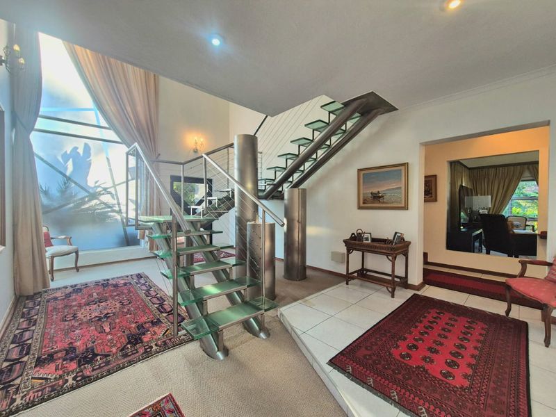 Spacious entrance hall featuring a modern glass staircase with stainless steel balustrades, double volume ceilings, and large windows allowing for abundant natural light.