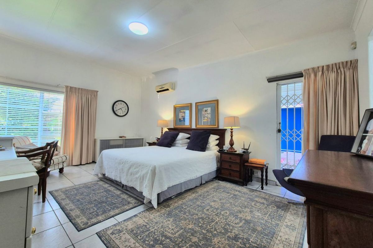Spacious bedroom featuring tiled flooring, a split-system air conditioner, and direct access to the exterior through a sliding glass door with a security gate.