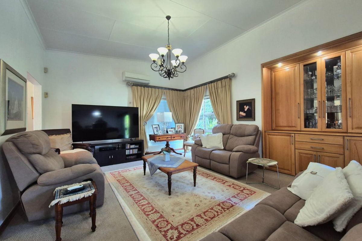 A comfortable living room featuring built-in wooden cabinetry, a classic chandelier, and a split-system air conditioner, offering a warm and functional space.