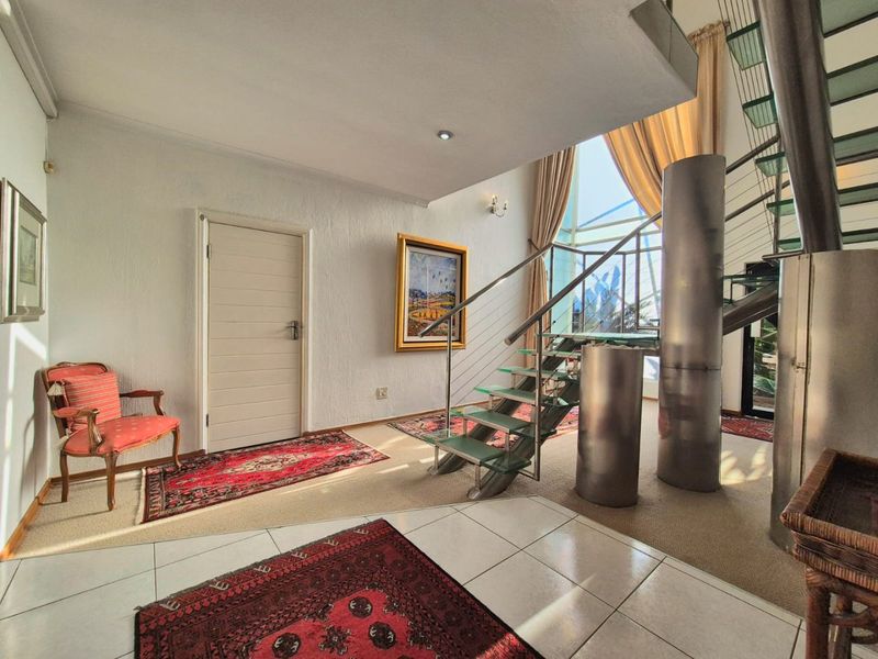 Spacious entrance hall featuring a modern glass staircase with stainless steel balustrades, large windows, and a combination of tiled and carpeted flooring.