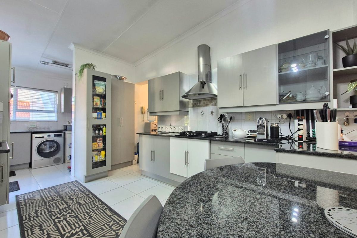 A functional kitchen featuring granite countertops, a gas hob with stainless steel extractor, and integrated cabinetry with an adjoining laundry space.