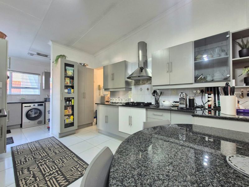 A functional kitchen featuring granite countertops, a gas hob with stainless steel extractor, and integrated cabinetry with an adjoining laundry space.