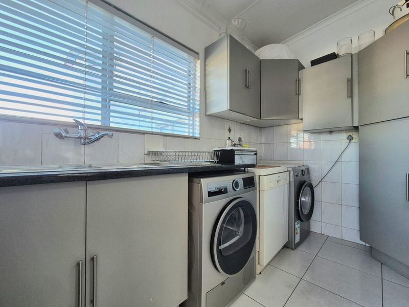 A functional laundry room featuring built-in cabinetry, tiled backsplash, and space for multiple appliances, providing a practical utility area.