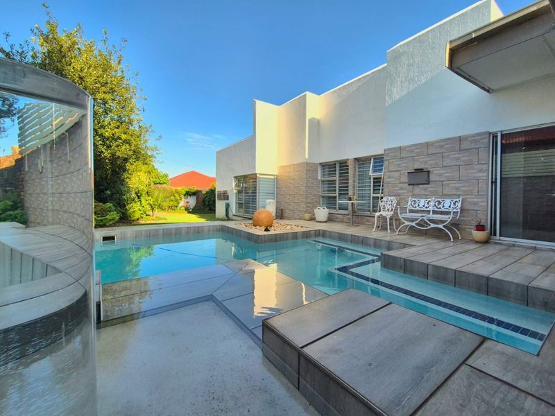A well-maintained outdoor pool area featuring modern tiled decking, stone wall accents, and direct access to the home through sliding glass doors.