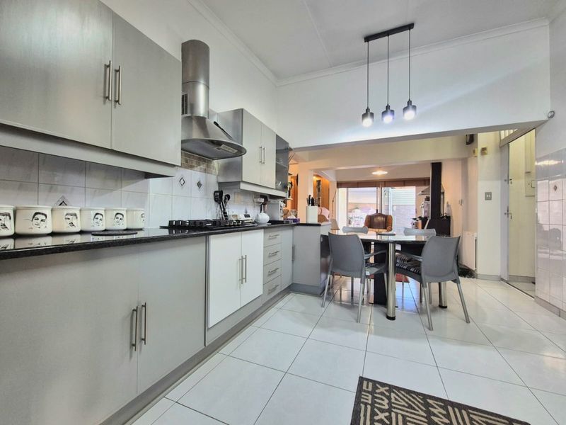 Modern open-plan kitchen featuring sleek grey cabinetry, granite countertops, and a gas hob, seamlessly flowing into the dining area with tiled flooring throughout.