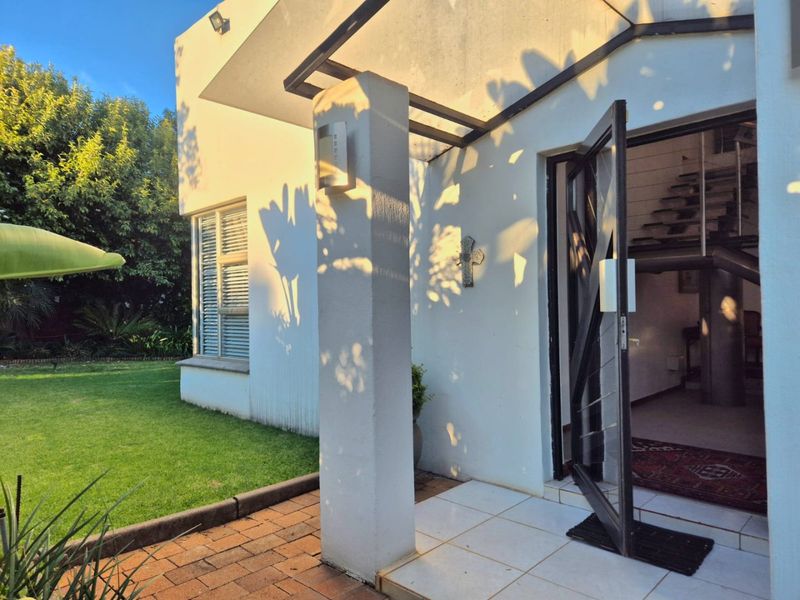 A bright front entrance featuring a tiled porch, modern metal-framed glass door, and a view into the home's interior staircase.