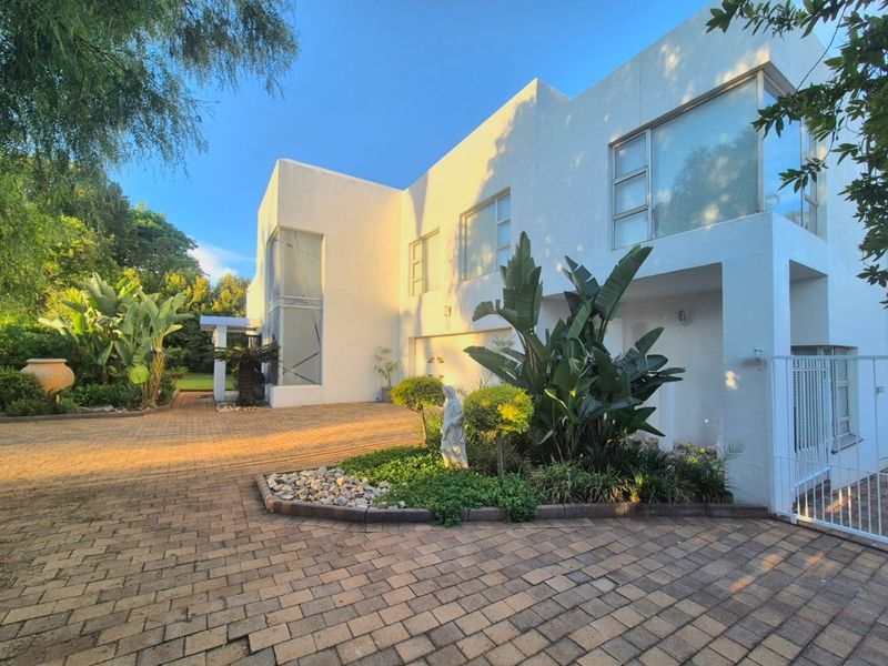 Modern double-storey residence featuring a clean white facade, large windows, and a spacious paved driveway with established garden landscaping.