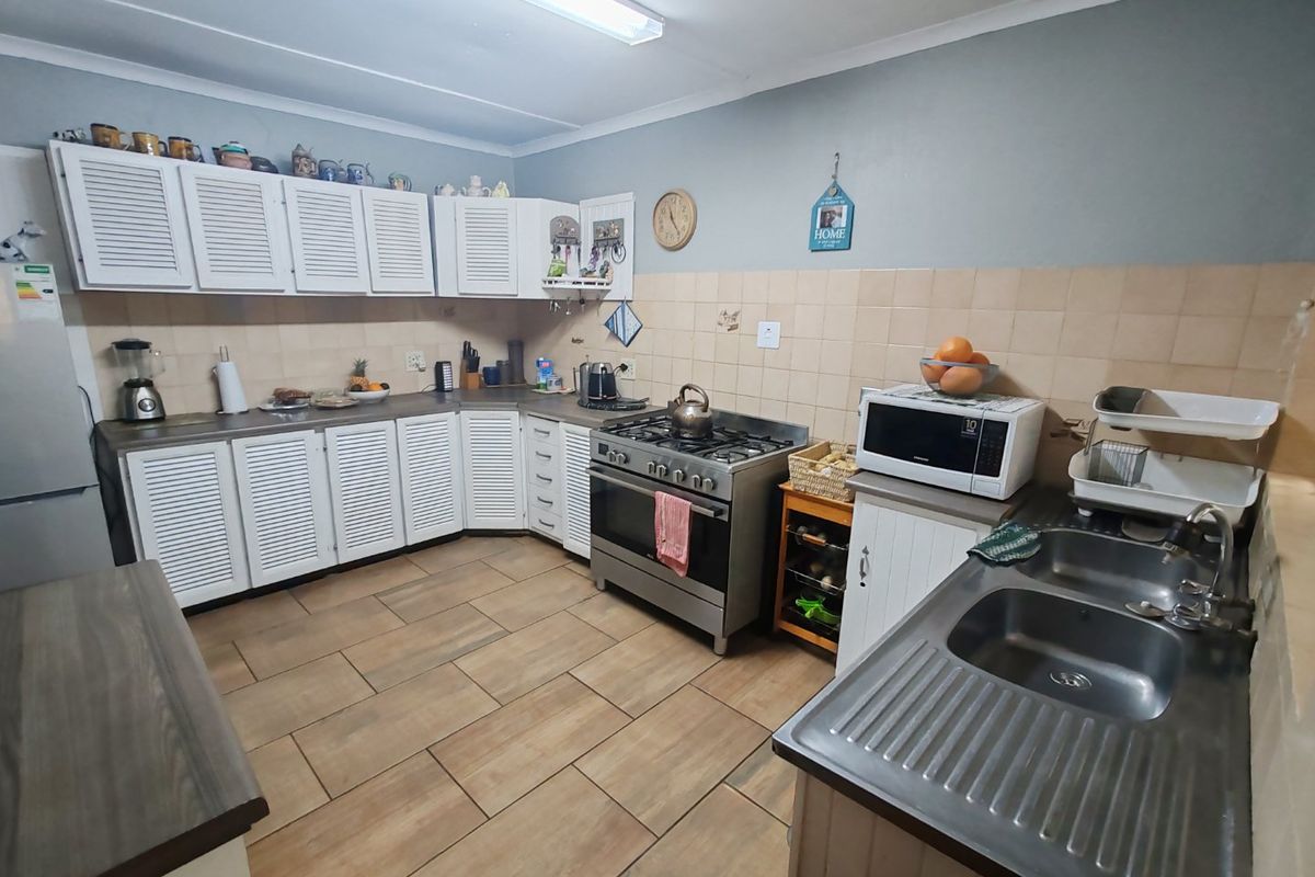 Functional kitchen featuring louvered cabinetry, stainless steel gas stove, double bowl sink, and tiled backsplash with neutral ceramic flooring.