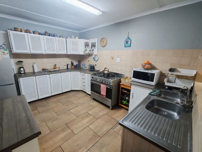 Functional kitchen featuring louvered cabinetry, stainless steel gas stove, double bowl sink, and tiled backsplash with neutral ceramic flooring.