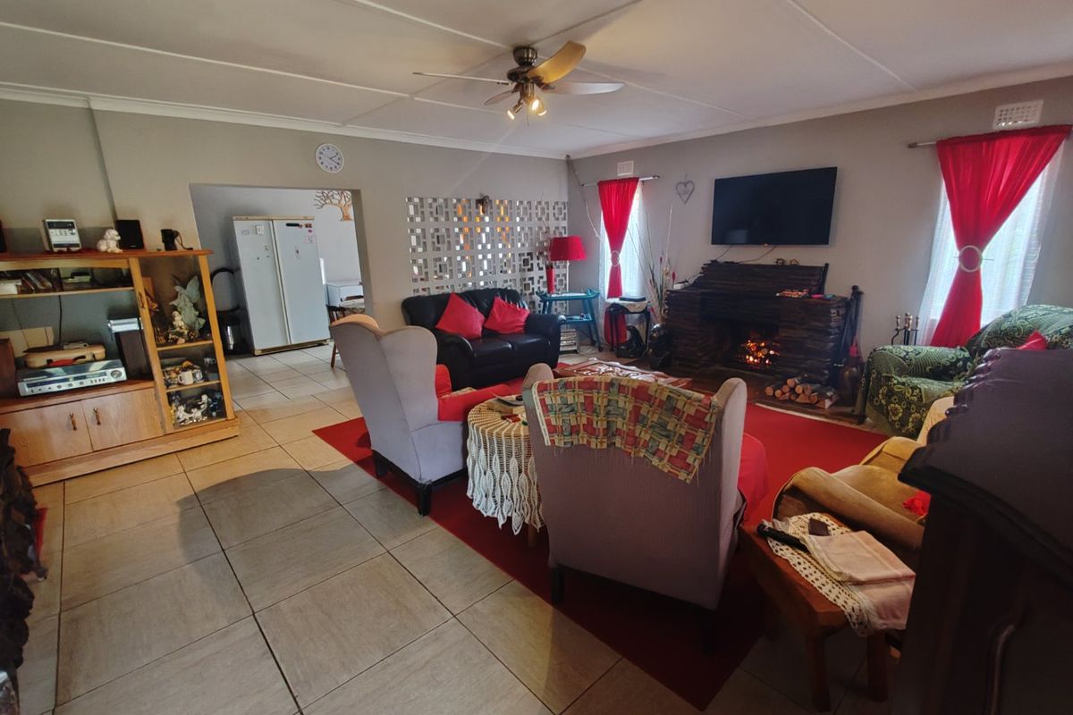 Spacious living room featuring a stone fireplace, tiled flooring, and a ceiling fan, with an open transition to the adjacent kitchen area.