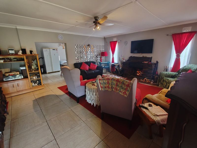 Spacious living room featuring a stone fireplace, tiled flooring, and a ceiling fan, with an open transition to the adjacent kitchen area.