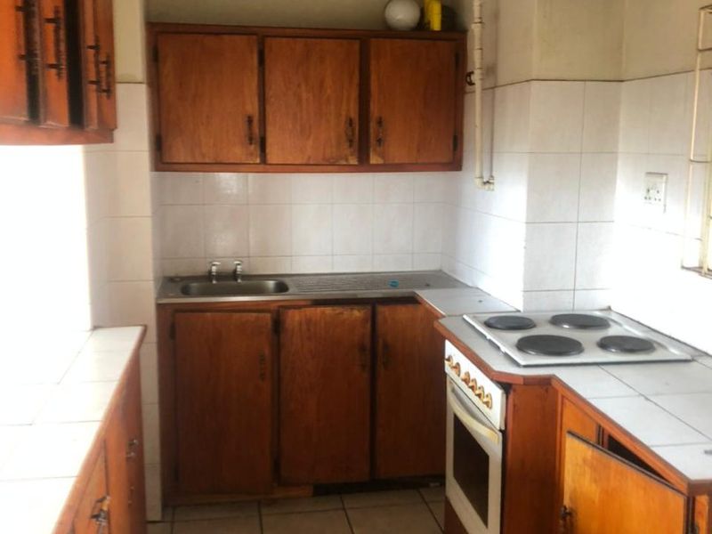 A dated kitchen featuring wooden cabinetry, tiled countertops, and built-in appliances, offering significant potential for modernization and renovation.