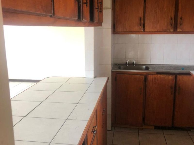A dated kitchen featuring wooden cabinetry, tiled countertops, and a stainless steel sink, offering significant potential for a modern renovation.