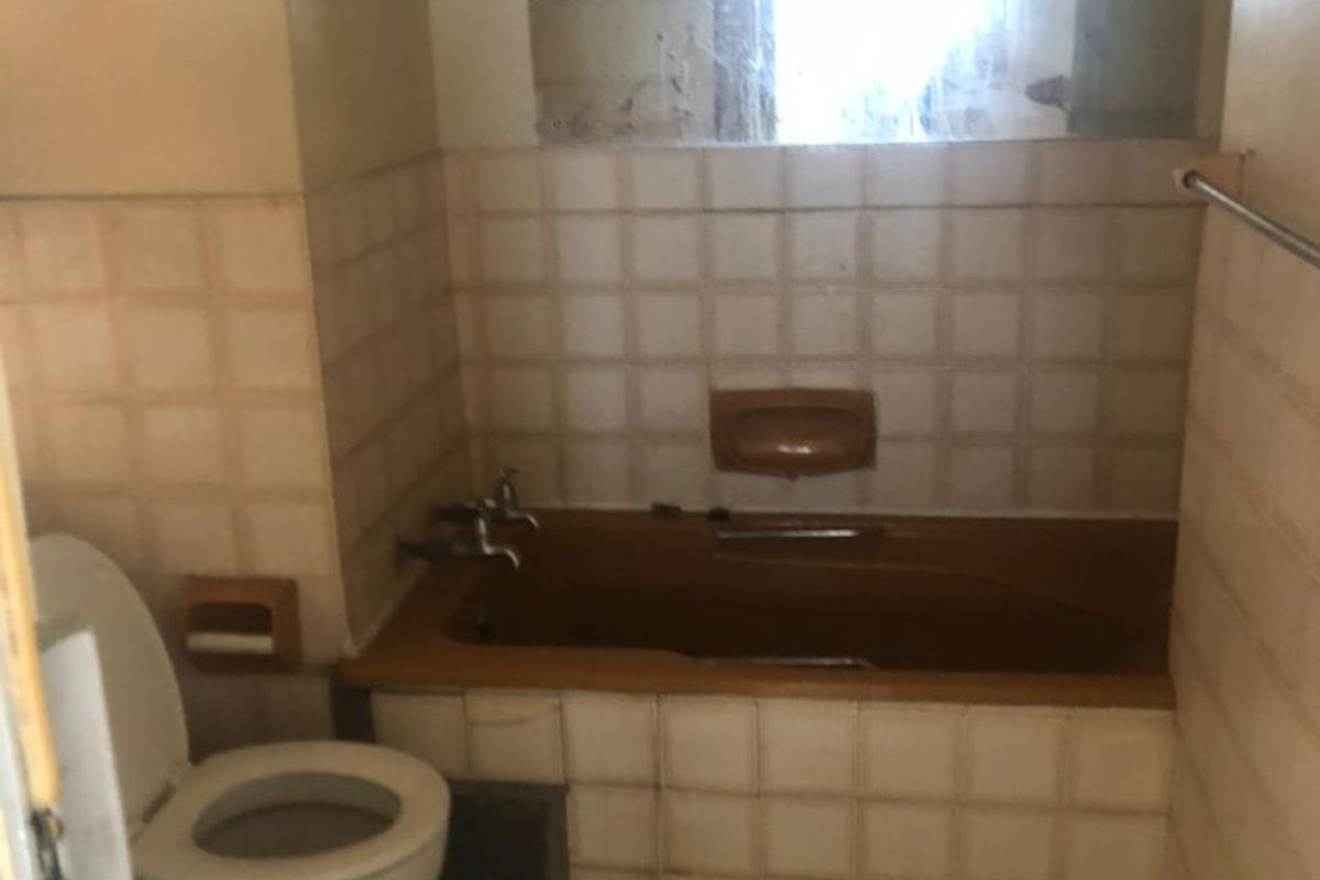 A dated bathroom featuring a built-in bathtub, toilet, and tiled finishes, offering significant potential for a modern renovation.