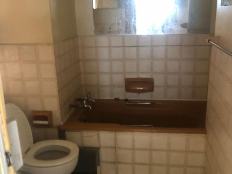A dated bathroom featuring a built-in bathtub, toilet, and tiled finishes, offering significant potential for a modern renovation.