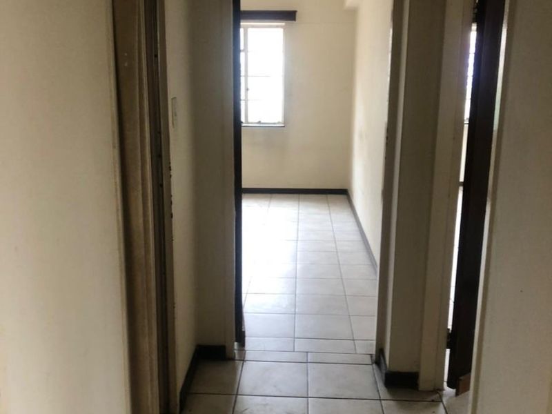 A vacant hallway featuring tiled flooring and access to adjacent rooms, showing signs of wear and requiring cosmetic updates.