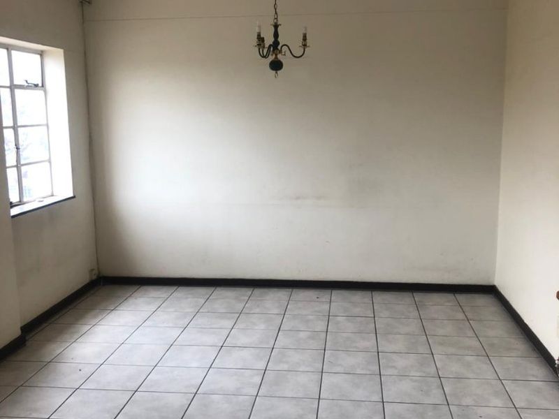 An empty living room featuring ceramic floor tiles, a multi-pane window, and a central ceiling light fixture, ready for renovation or staging.
