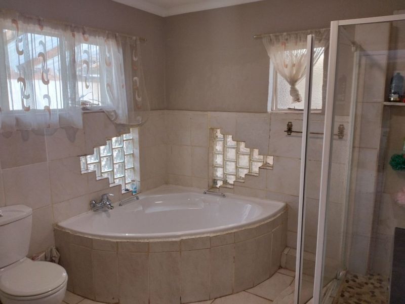 A functional bathroom featuring a corner bathtub, a glass block feature wall, a separate shower enclosure, and neutral tiled finishes.