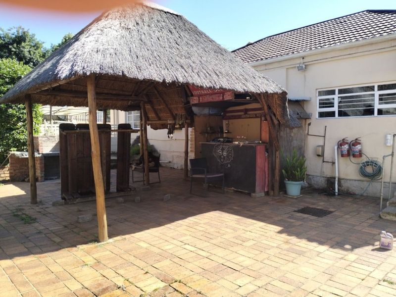 Outdoor entertainment area featuring a thatched roof lapa, brick paving, and a built-in bar structure.