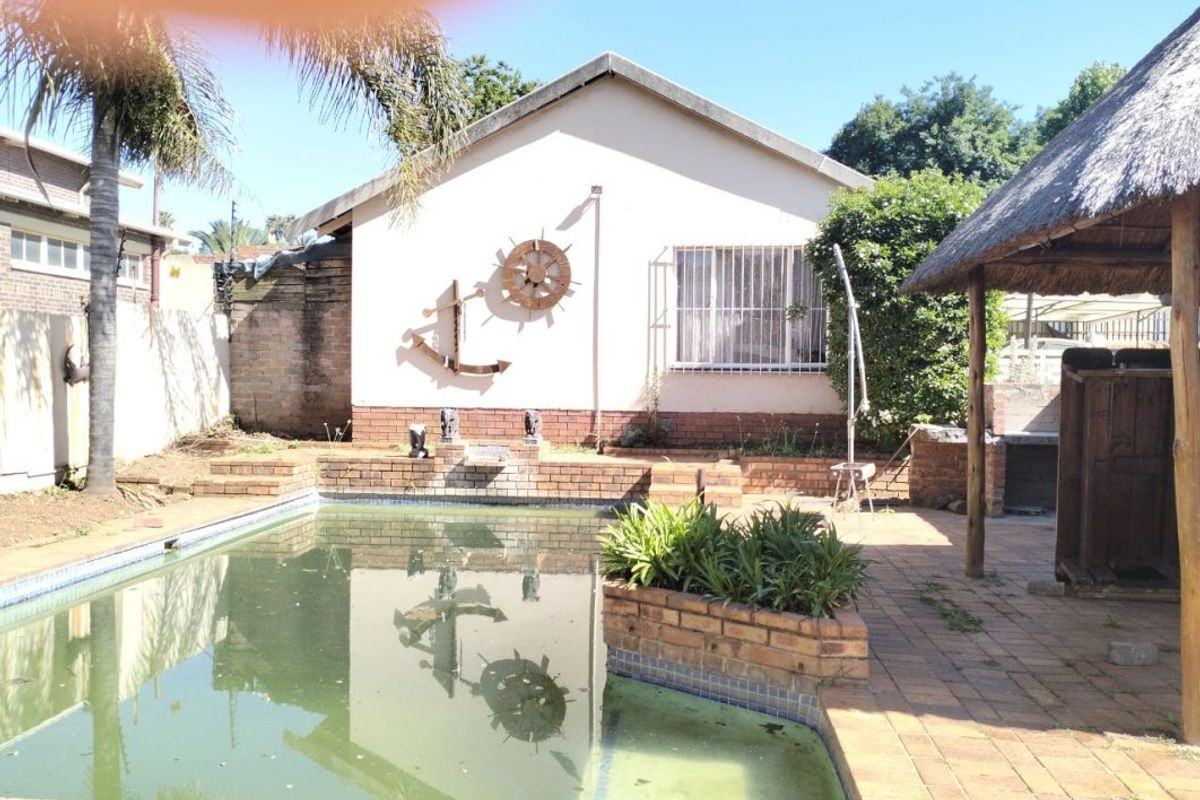 Rear garden area featuring a swimming pool, brick paved patio, and a thatched lapa with a built-in braai.