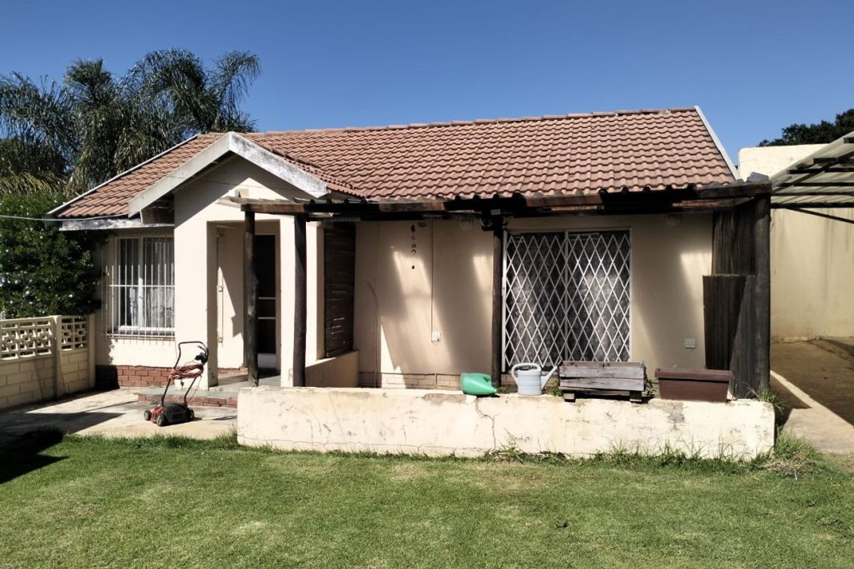 Rear view of the house featuring a tiled roof, a timber pergola structure, and a concrete low wall bordering the garden area.