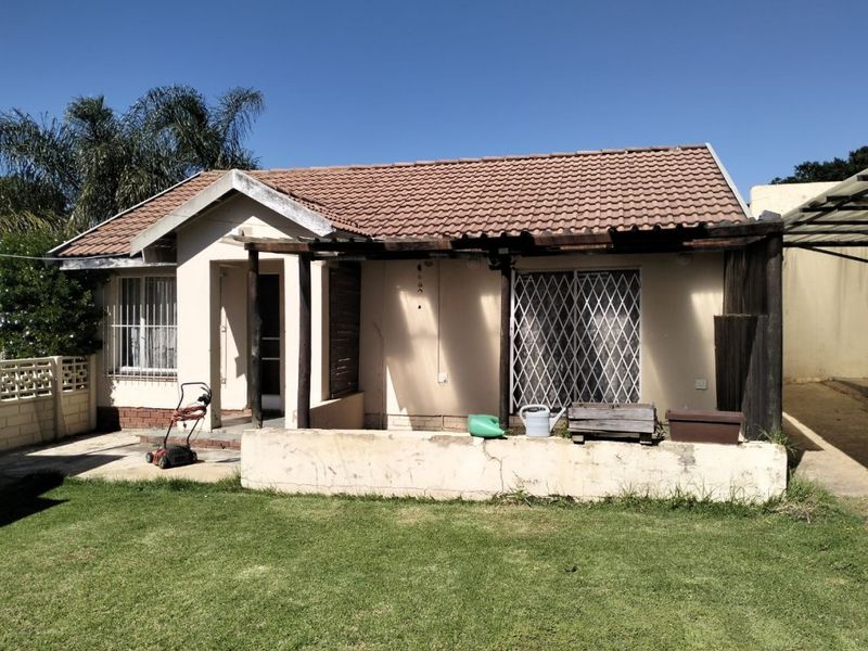 Rear view of the house featuring a tiled roof, a timber pergola structure, and a concrete low wall bordering the garden area.
