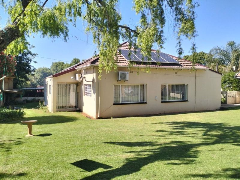Rear view of a residential house featuring a well-maintained lawn, tiled roof with solar panels, and exterior air conditioning unit.