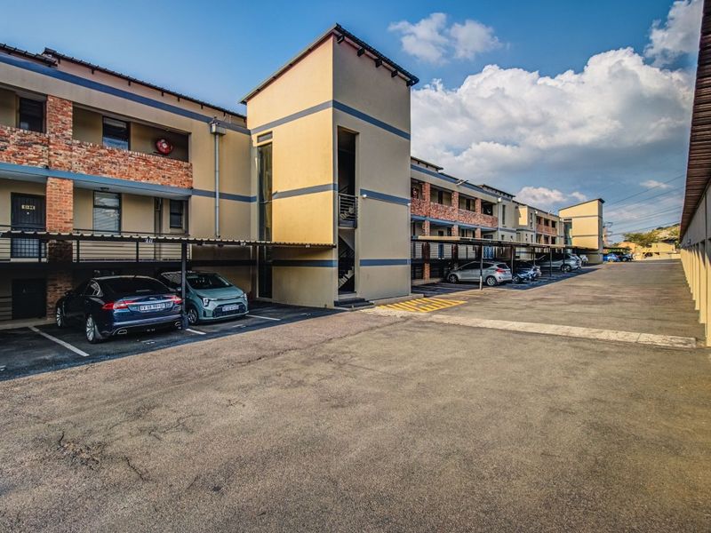 Exterior view of an apartment complex featuring covered parking bays, a multi-story stairwell tower, and brick facade accents.