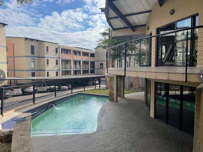 Communal pool area featuring a paved deck, covered patio space, and balcony access within a modern apartment complex.