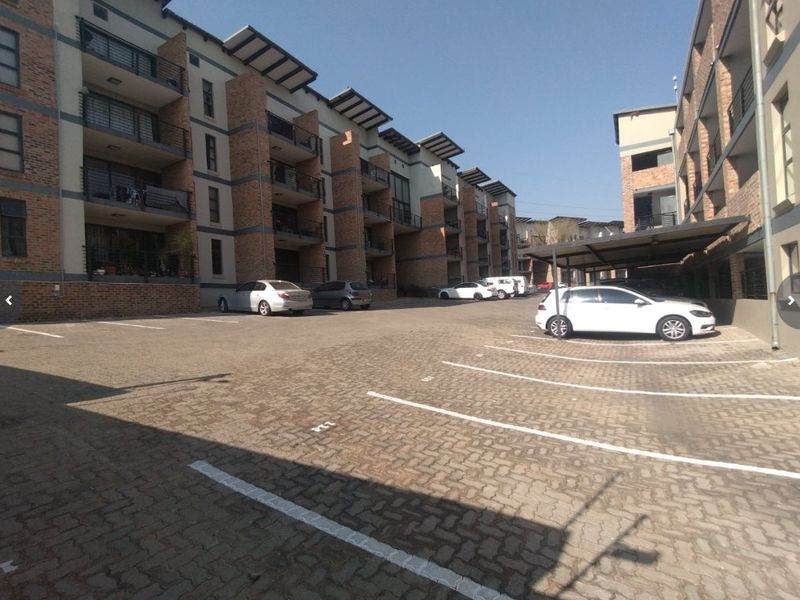 Exterior view of a multi-story apartment complex featuring brick facade detailing, private balconies, and a paved parking area with covered bays.