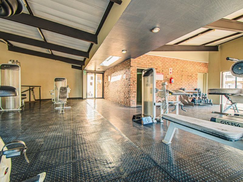 A spacious gym facility featuring exposed brick walls, high ceilings with exposed beams, durable rubber flooring, and natural light from a skylight.