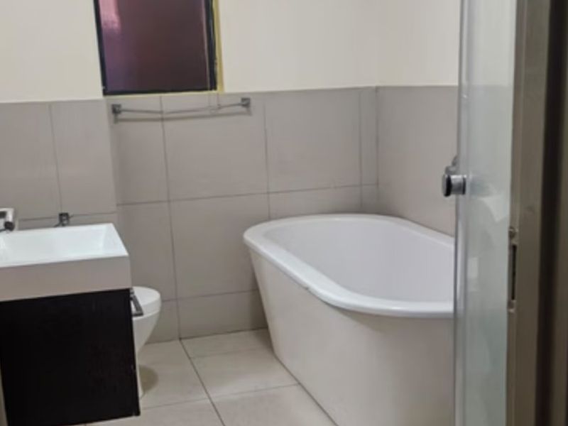 A clean, modern bathroom featuring a freestanding bathtub, wall-mounted vanity, and neutral ceramic tiling throughout.