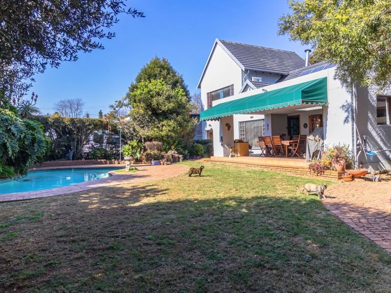 Rear view of the property featuring a swimming pool, brick-paved patio area, and a retractable awning providing shade to the outdoor living space.