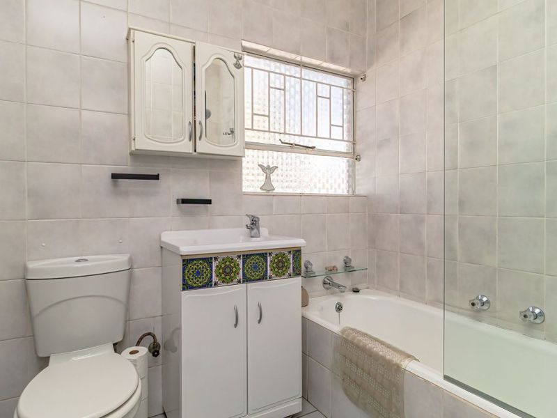 A functional bathroom featuring a bathtub with a glass screen, a vanity unit, and a toilet, finished with neutral wall tiles.