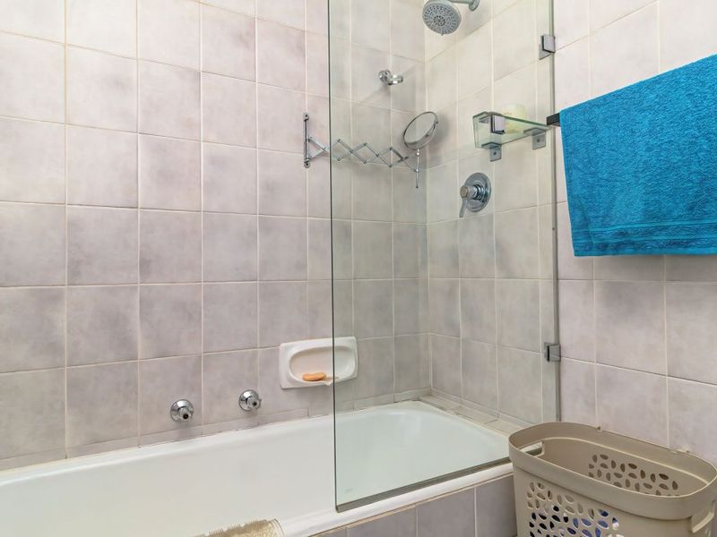 A functional bathroom featuring a built-in bathtub with a glass shower screen, wall-mounted shower head, and neutral tiled finishes.