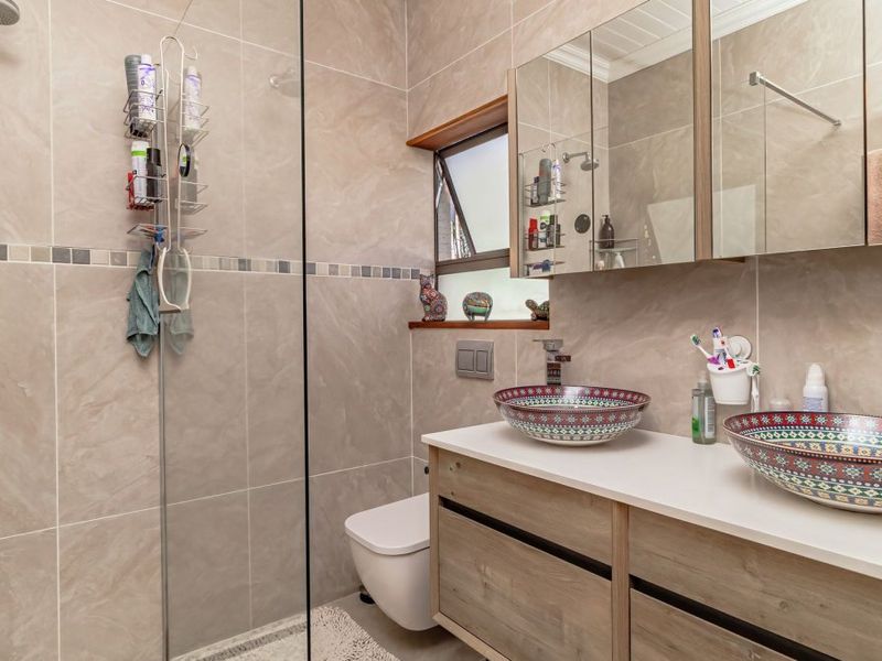 Modern bathroom featuring a double vanity with decorative vessel sinks, a walk-in shower with glass screen, and a wall-mounted toilet.