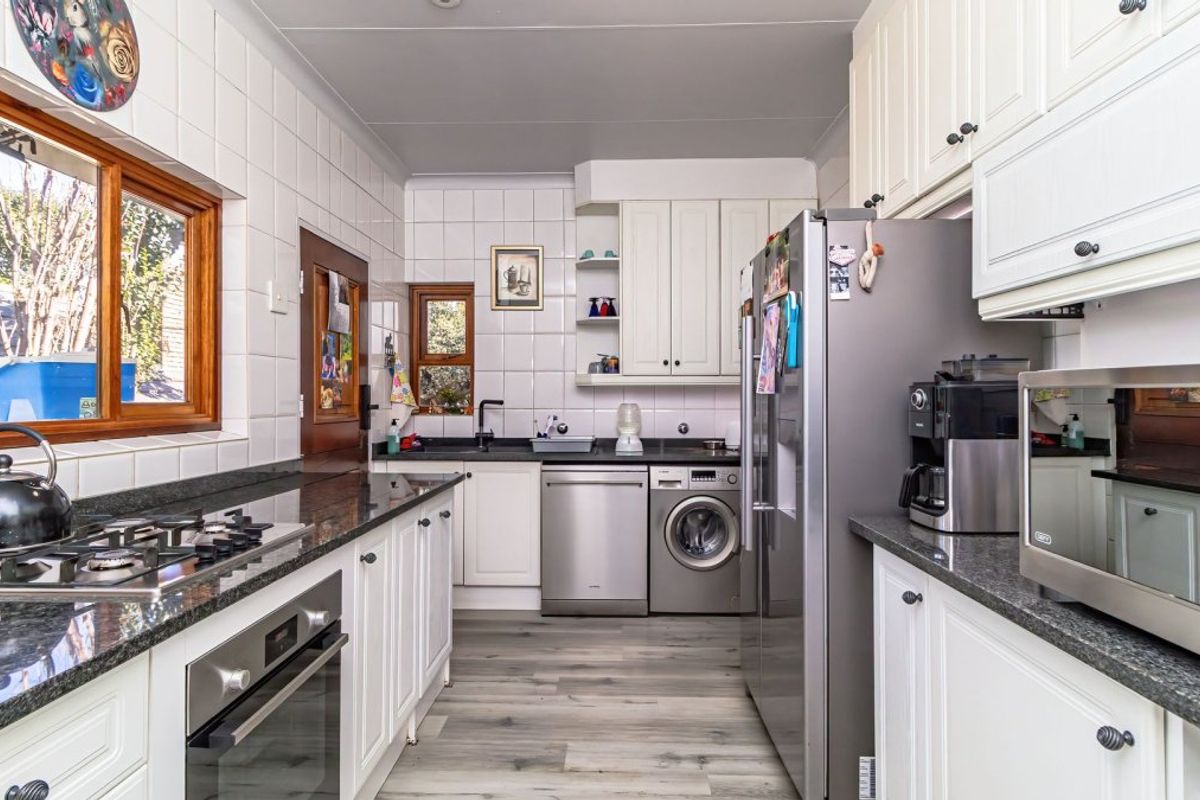 A functional kitchen featuring white cabinetry, granite countertops, a gas hob, built-in oven, and integrated laundry appliances, finished with tiled splashbacks and laminate flooring.