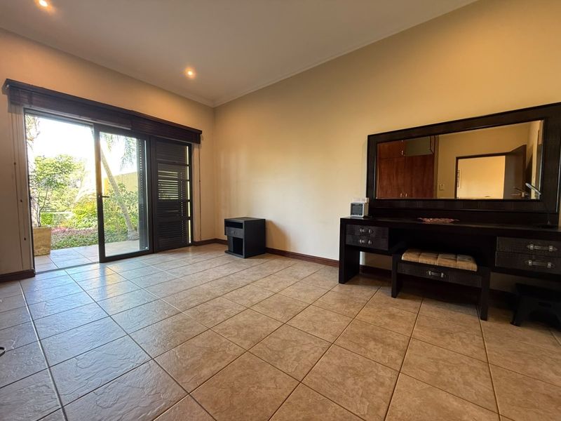 Spacious bedroom featuring tiled flooring, recessed lighting, and a large sliding glass door providing direct access to the outdoor garden area.